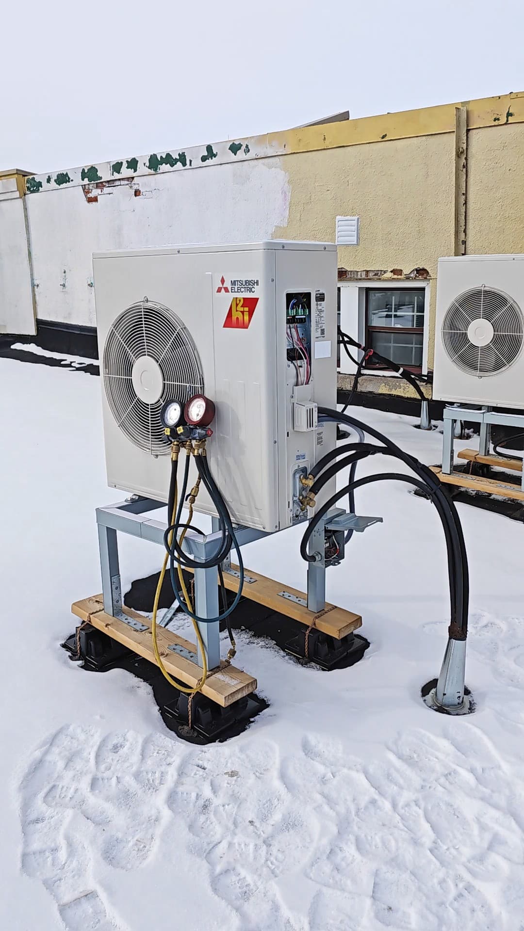 Outdoor heat pumps on a snow-covered roof, with manifold gauges connected to the nearer unit