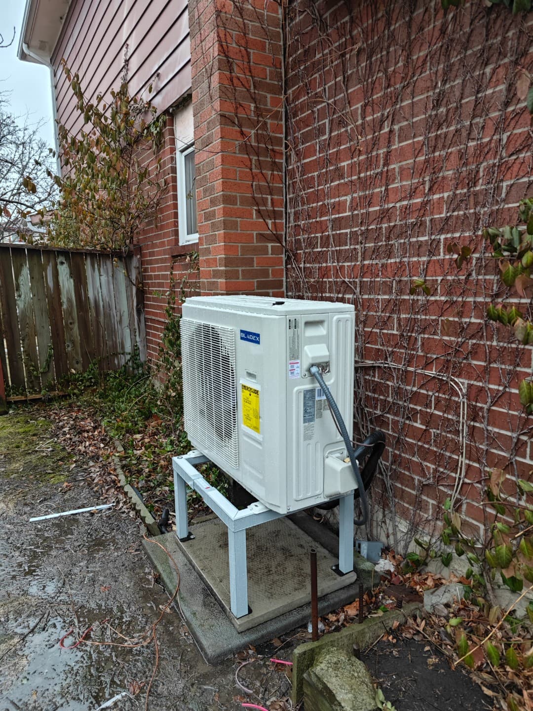 White outdoor heat pump on a stand beside a brick wall