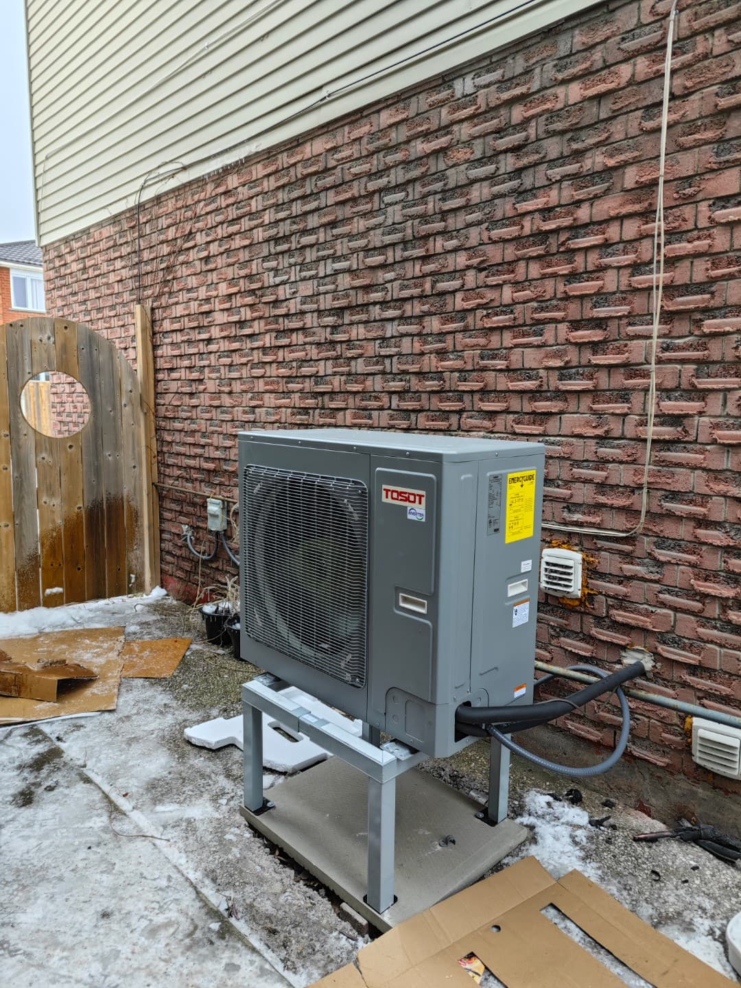 Gray outdoor heat pump on a stand with snow on the ground