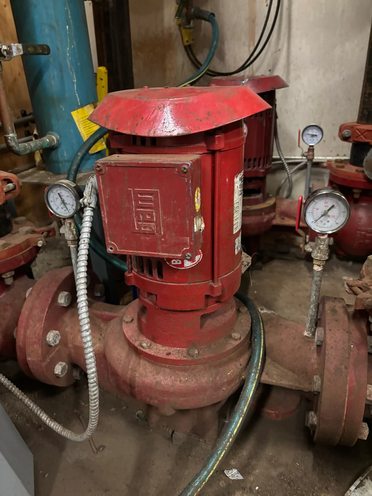 Two red vertical circulation pumps with pressure gauges in a mechanical room