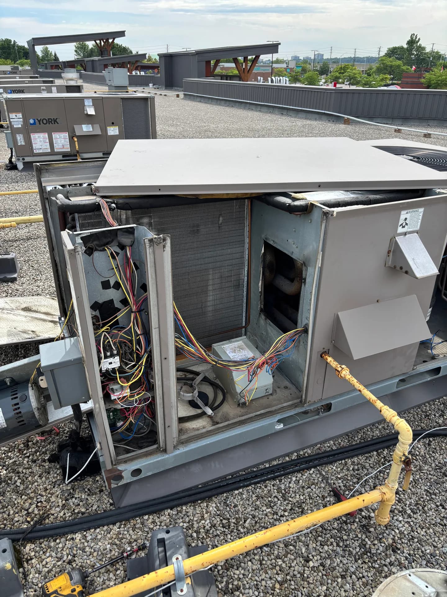 Open commercial rooftop HVAC unit on a gravel roof, with a second unit and gas piping nearby