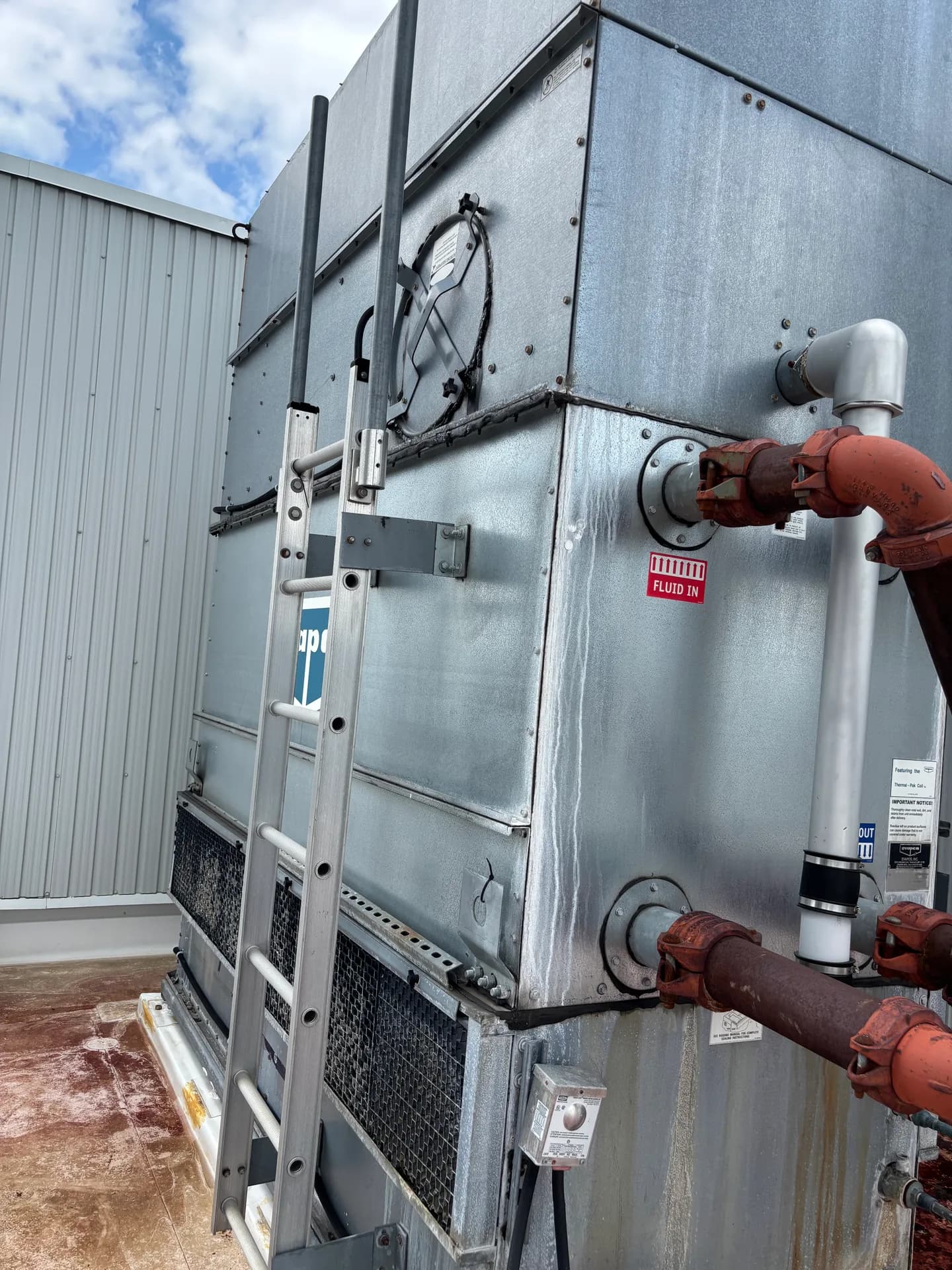 Close view of a cooling tower with an access ladder and fluid piping