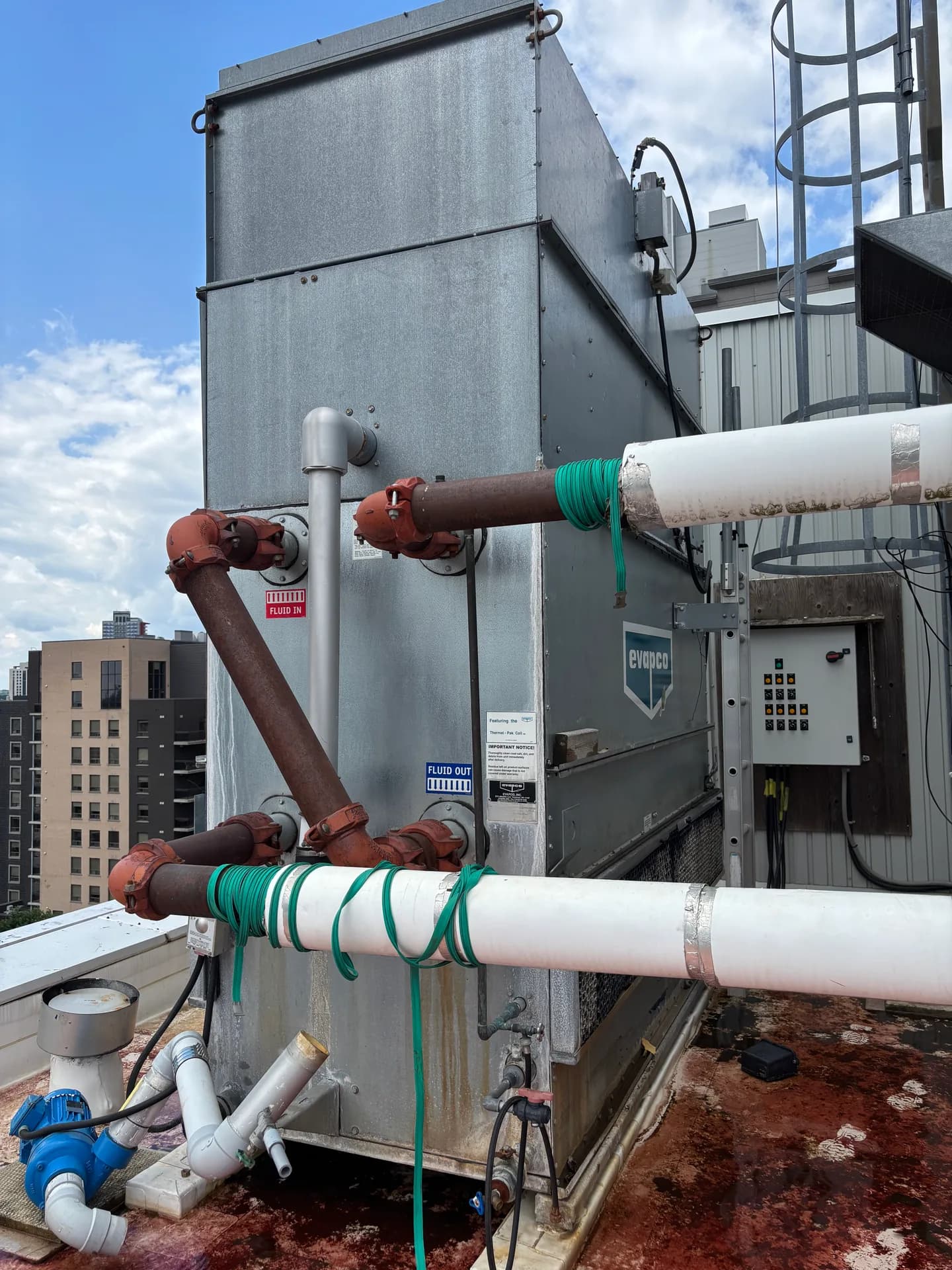 Galvanized cooling tower on a roof with connected piping and a control cabinet